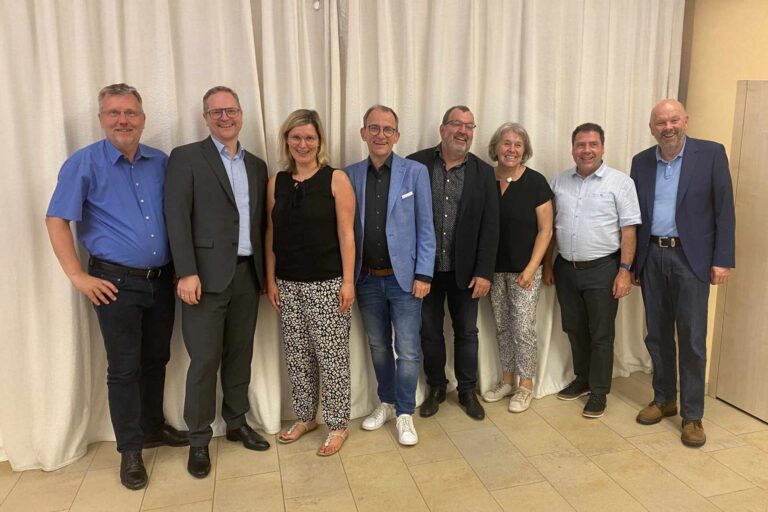 Gruppenfoto der Vorstandschaft der ChristusBewegung Lebendige Gemeinde mit neuem Geschäftsführer – Übergabe im Oktober 2024, festlicher Moment mit acht Personen vor hellem Vorhang.