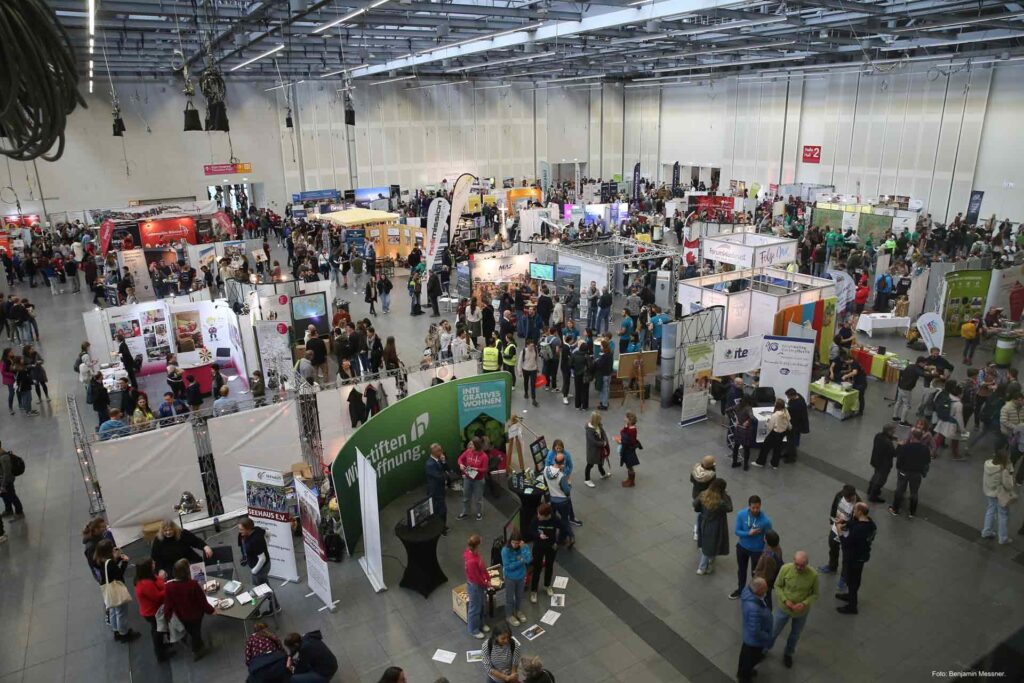 Große Messehalle mit zahlreichen Ständen und Besuchern auf der JUMIKO 2023 – christliche Jugendmissionskonferenz mit Infoständen, Organisationen und reger Beteiligung.