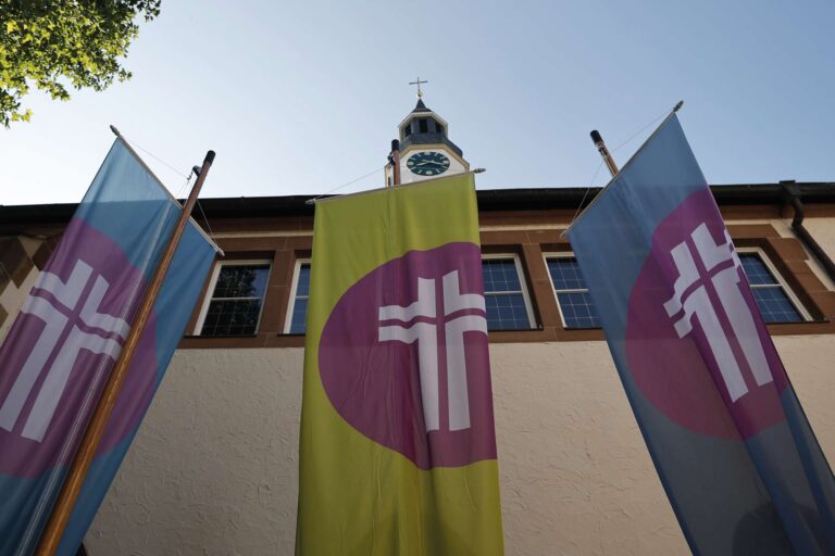 Blick auf eine Kirche mit drei Fahnen mit Kreuzsymbol vor dem Gebäude – Aufnahme zur Sommersynode 2025 der ChristusBewegung mit evangelischem Bezug.