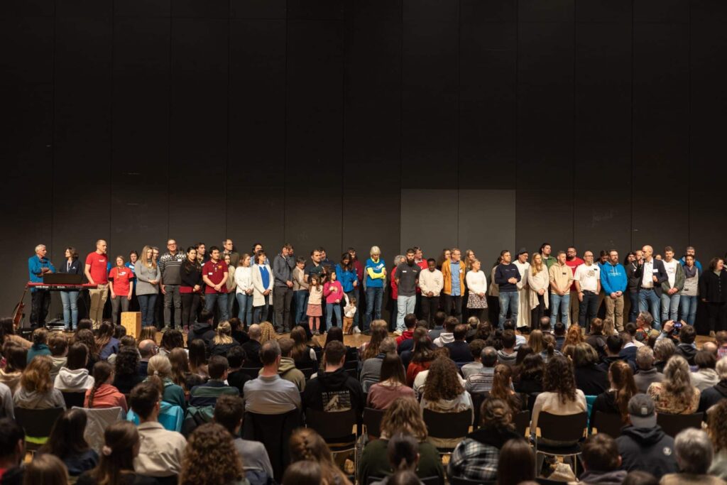 Gruppenfoto auf der Bühne bei einer christlichen Jugendkonferenz – zahlreiche Mitarbeitende stehen vor einem großen Publikum während einer Veranstaltung wie der Jumiko.